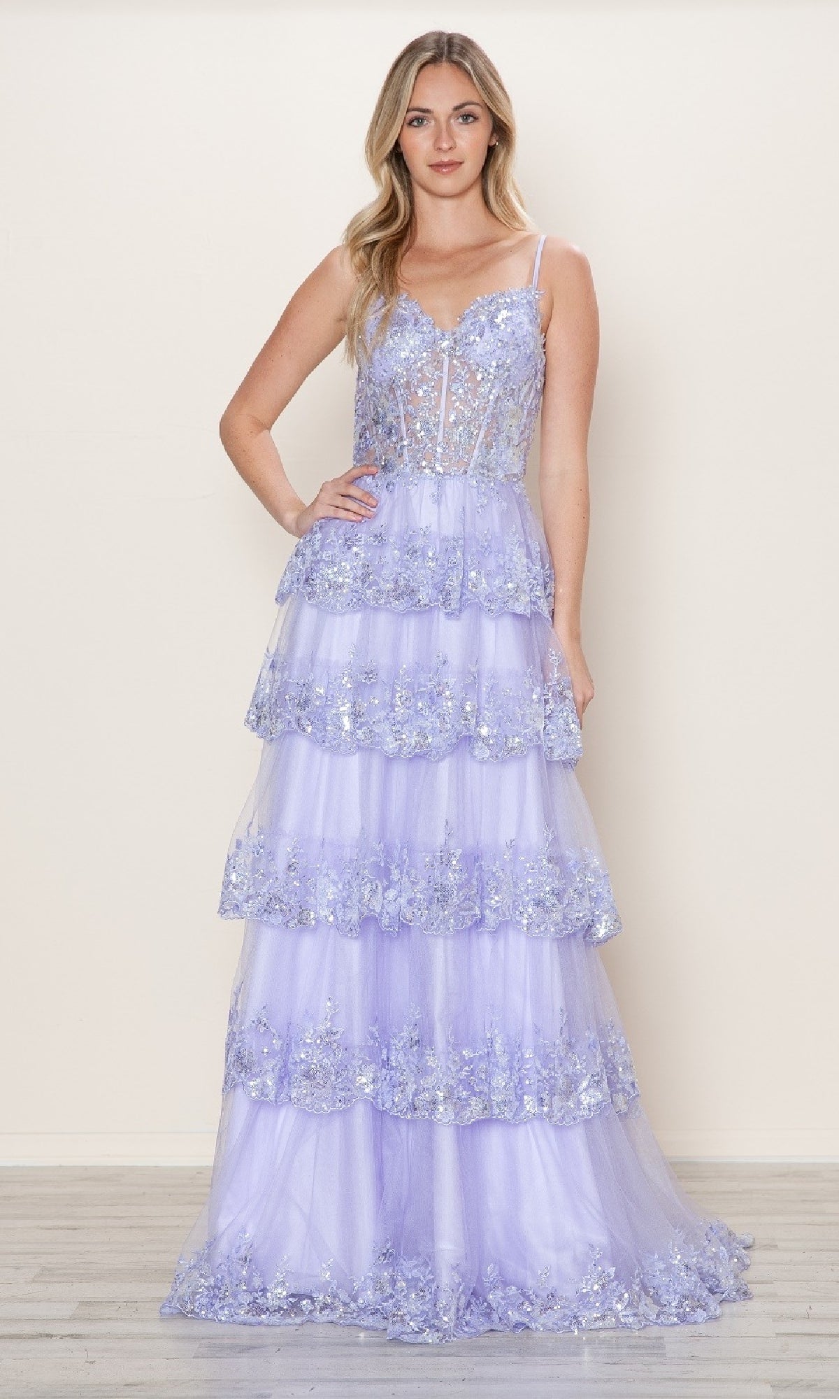 A woman wears the Long Glitter-Lace Tiered Prom Dress (Poly USA 9548), a floor-length lavender gown with spaghetti straps, floral embellishments, and a sheer bodice.